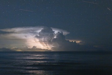 Thunderstorm cell over the sea at night with visible stars in the sky, creating a dramatic scene