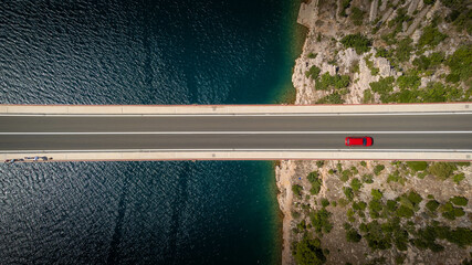 Top down view of a red car alone driving on a bridge over the sea. Background images for travel,...