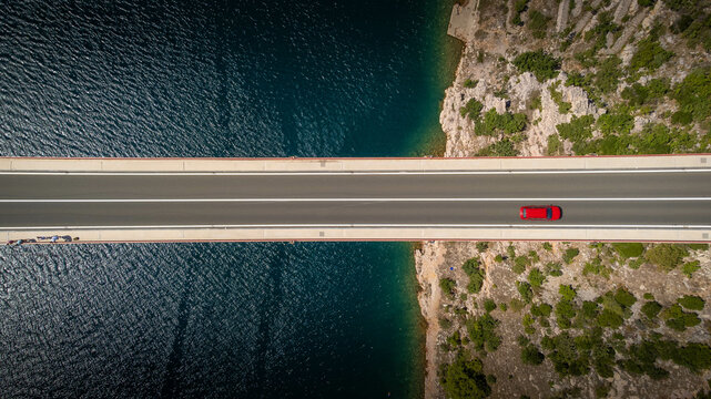 Top down view of a red car alone driving on a bridge over the sea. Background images for travel, holidays, the beauty of traveling by car to discover a country. Maslenica bridge, Croatia.
