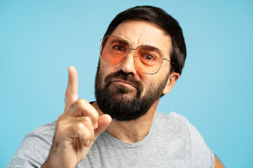 Serious man pointing finger wearing sunglasses on blue background