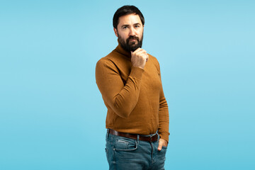 Pensive mature man touching beard and thinking on blue background