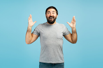 Excited bearded man showing surprise and excitement raising hands in amazement on blue background