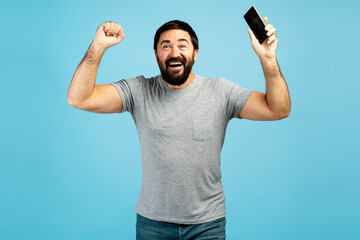 Excited man celebrating success holding smartphone on blue background