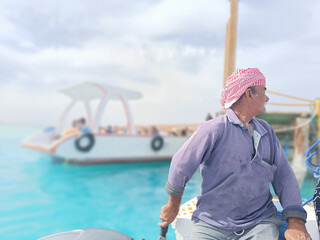 Fototapeta premium Old Sailor in the Sea Riding and Sailing with his Boat An old sailor with a white with a white mustache who is wearing a Bedouin Scarf on his head