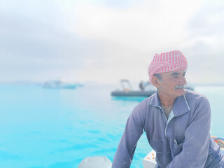 Old Sailor in the Sea Riding and Sailing with his Boat An old sailor with a white with a white mustache who is wearing a Bedouin Scarf on his head