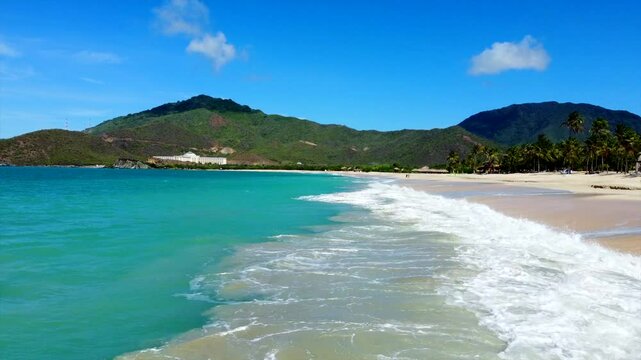 A beautiful beach with a blue ocean and a mountain in the background. The beach is empty and the water is calm