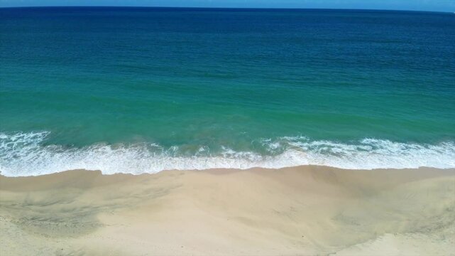 The ocean is calm and the sky is blue. The beach is empty and the waves are small