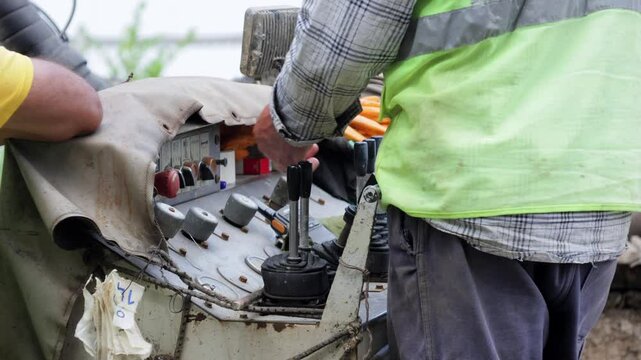 A close-up view of a worker operating construction machinery. Hands are seen manipulating the levers and joysticks, showcasing the precise control needed for construction tasks.