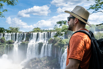 Hombre turista con sombrero y gafas de sol contemplando las cataratas del Iguazú, en el Parque Nacional Iguazú, Argentina