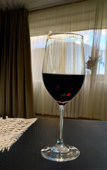 Glass of red wine on a dark table against the background of beige curtains on the window