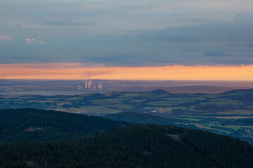 distant view of industrial chimneys smoking near electric windmills at dawn