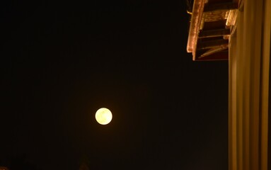 full moon floating on sky behnd yellow building in night background