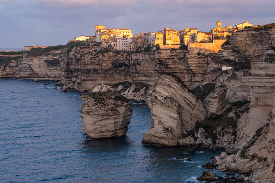 Sonnenaufgang in Bonifacio, Korsika, die H&auml;user auf der steilen Felsenklippe werden von der warmen Sonne angeleuchtet, im Vordergrund liegen die hellen Kreidefelsen im Meer