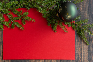 Red Christmas paper card, with space for text decorated with a Christmas tree branch and a green Christmas bauble