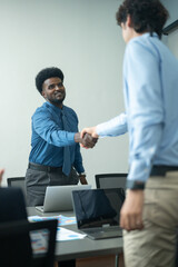 Two professionals shaking hands in an office setting, symbolizing agreement, partnership, or successful collaboration during a business meeting.  