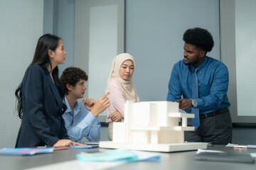 Diverse group of professionals engaged in a discussion around an architectural model during a collaborative project planning session in an office. 