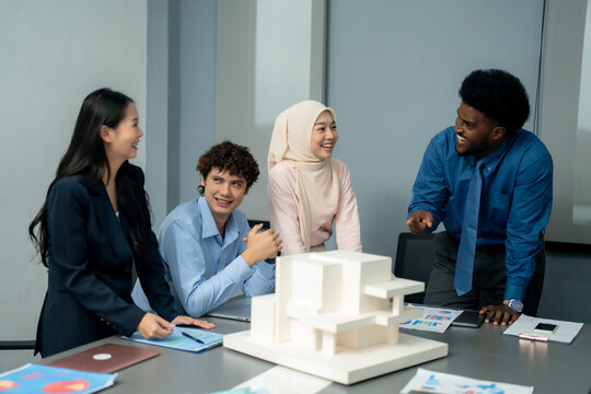Group of professionals engaged in a lively discussion around an architectural model, sharing ideas and collaborating in a modern office. 
