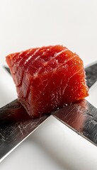 Fresh, high-quality tuna steak delicately placed on two stainless steel knives.