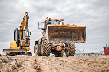 Heavy machinery working on a construction site under a cloudy sky, moving earth as the day begins...
