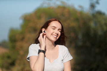 Beautiful young woman smiles happily while listening to music with her airphones while walking in the park