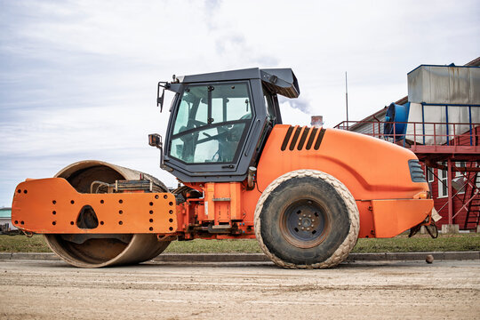A powerful orange road roller prepares to smooth out a construction site under cloudy skies in the heart of urban development - Powered by Adobe