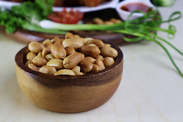 Light brown roasted peanuts, shelled, placed in a light dark wooden bowl. Place the bottom of the tray on the food and vegetables. On the marble dining table

