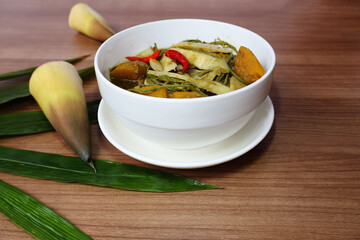 Bamboo shoot, pumpkin, vegetable curry, place chilli on top green thick juice In a bowl with a white saucer Placed on a brown wooden table

