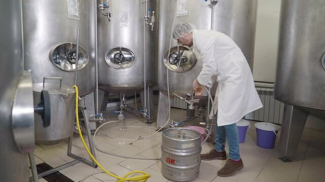 Small barrel with ale with a huge tube at production facility. Detaching the tube from the barrel with ale in production room. Filling up the containers with ale from the barrel at a production plant.