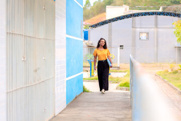 Estudante negra feliz chegando à faculdade. Ela está caminhando e sorrindo enquanto carrega cadernos e pastas na área externa da universidade. 