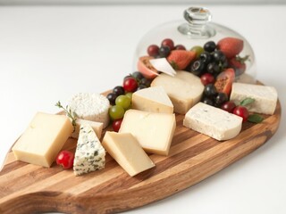 Wooden cheese board with glass dome showcasing assortment of cheese and fruits, elegant