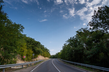 Fototapeta premium Road turn. Landscape highway, forest, mountains and sky on the horizon. Empty long mountain road to the horizon on a sunny summer day with dramatic cloudy sky. Highway turn panoramic view.