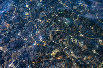 Underwater pebble backgrounds. Colorful stones sea bottom in the sun rays. View from above through clear water. Seascape wallpaper texture. Soft focus.