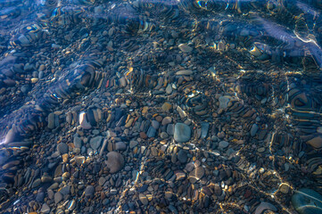 Underwater pebble backgrounds. Colorful stones sea bottom in the sun rays. View from above through clear water. Seascape wallpaper texture. Soft focus.