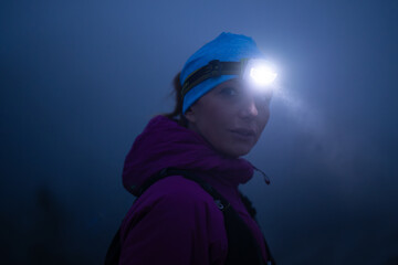 female Hiker or triathlon trail runner with a headlamp on a trail in the mountain with fog at night © .shock