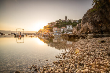Harbor and beach with an old village on a hill. Boats are reflected in the water, the sun rises on...