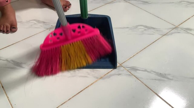 A broom sweeping debris into a blue dustpan on a tiled floor.