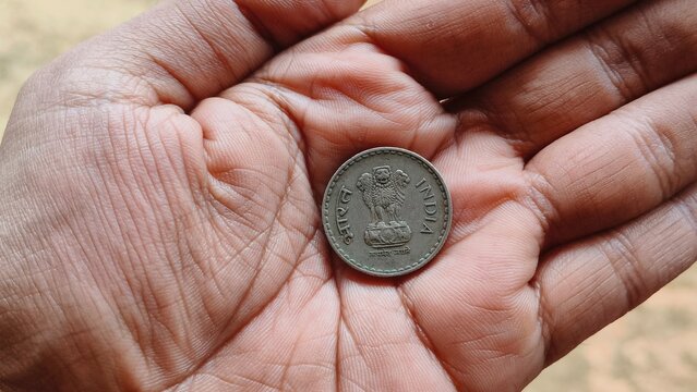 Indian state round metal coin with lion capital of ashoka national symbol or emblem lying in the hand palm of an adult worker. India culture unity, democracy and equality concept. Close up macro view.