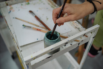 Artist dipping brush in blue paint on white table