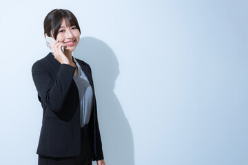 Business scene of young woman in suit making a phone call, light blue background
