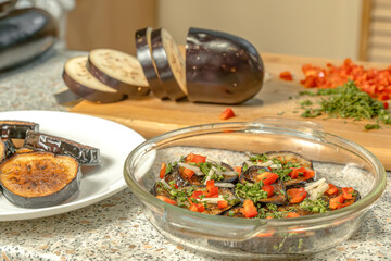 Fried eggplant slices sprinkled with pieces of sweet pepper, garlic and dill placed in a glass dish for further fermentation on. Home food. Close-up