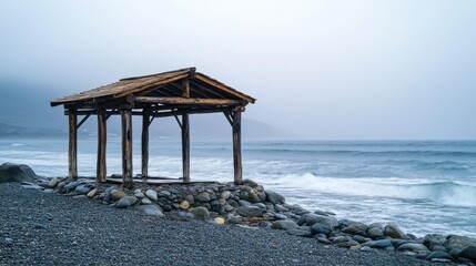 Small wooden gazebo with rustic charm, placed on a rocky beach, ocean waves nearby, overcast 