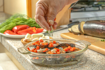 Chef sprinkles chopped garlic on fried eggplant slices placed in a glass dish for further fermentation. Home cooking. Close-up