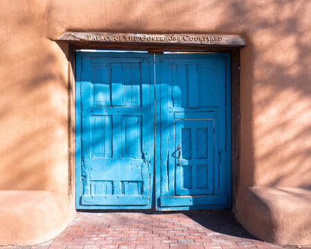 The royal blue wooden doors, adobe walls, and sign over the entrance to the Palace of the Governors Courtyard in Old Town Santa Fe, New Mexico