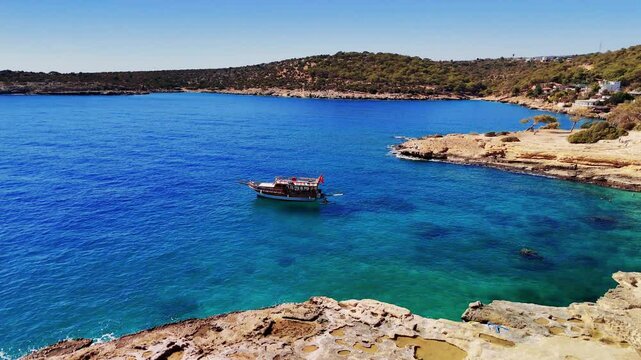 Traditional turkish gulet slowly navigates the stunning turquoise waters towards a picturesque rocky coastline, offering a mesmerizing view of the mediterranean sea