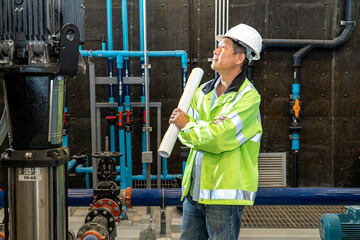 asian man worker in protective uniform and with hardhat using tablet for checking temperature in pipes Factory interior.