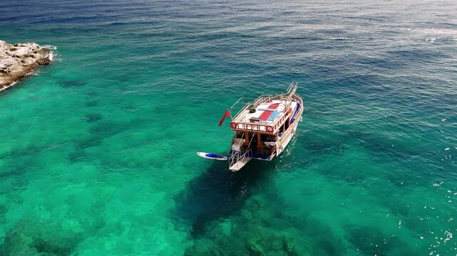 Traditional turkish gulet tourist boat floats on calm turquoise waters beside a rocky coastline, basking in the warm sunlight