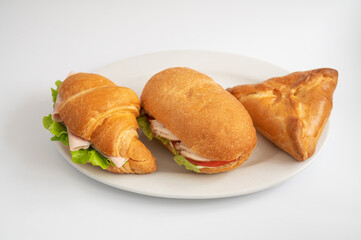 A plate with two croissant sandwiches, one baguette sandwich, and a savory pastry. Ideal for a light lunch or snack.