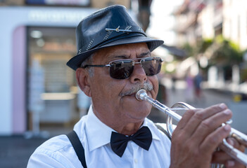 Portrait of jazz artist outdoors concert. Elderly man with black hat and sunglasses playing a...
