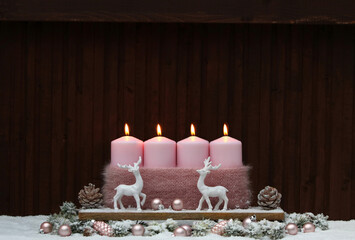 Vierter Advent:    Dekoration mit vier rosa Adventskerzen und Weihnachtsschmuck im Schnee vor einer...