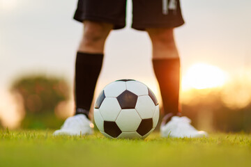 Soccer player with a ball. Action sport outdoors playing football for exercise at green grass field under the twilight sunset.